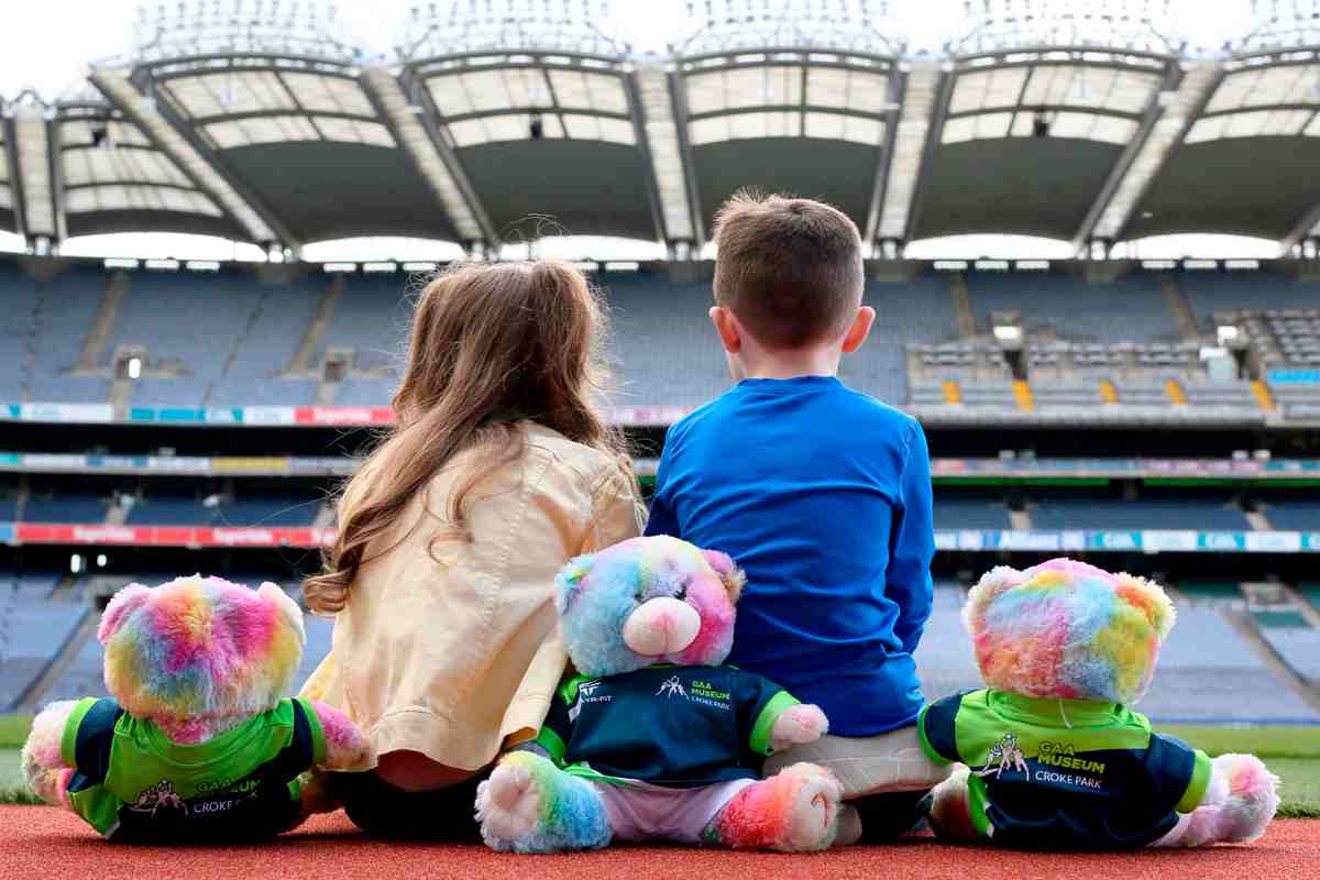 image of two children sitting with their backs turned, looking up at cusack stand in Croke Park with three colourful teddys bears